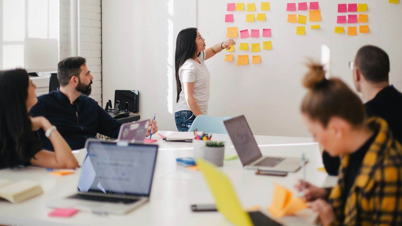 Three people around a small whiteboard covered with a short list of company names and sticky notes grouped by role.