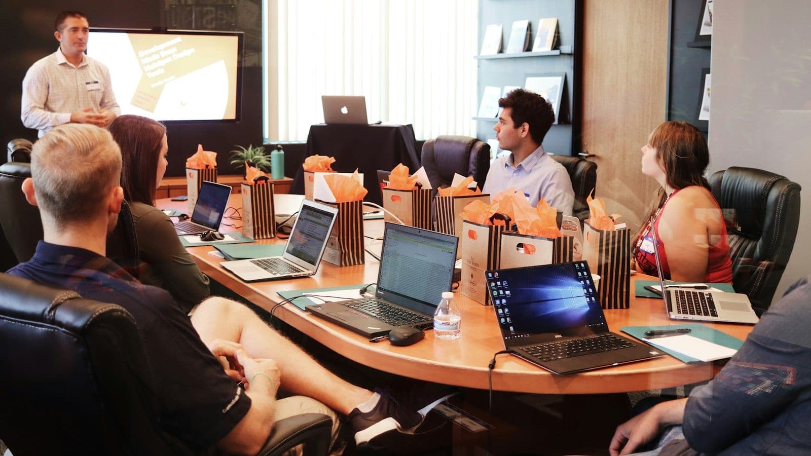 A CMO presenting a single pipeline chart on a wall screen to a small board meeting around a wooden table, with laptops and coffee cups in soft afternoon light